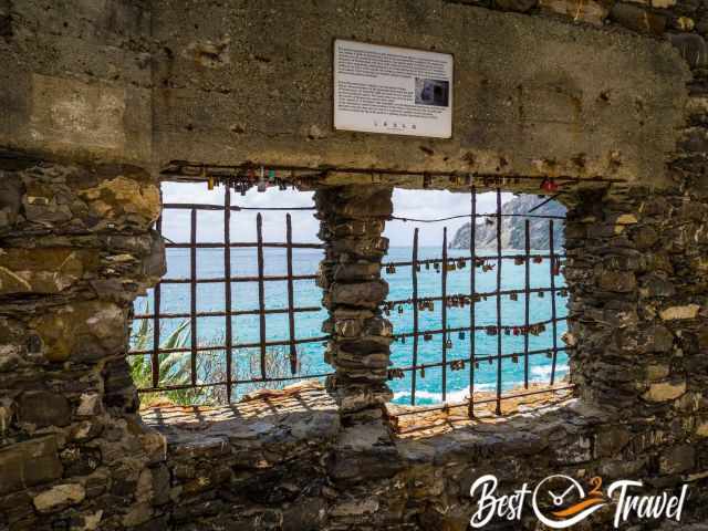 Ein vergittertes Denster in einer Ruine mit Blick auf das Meer.