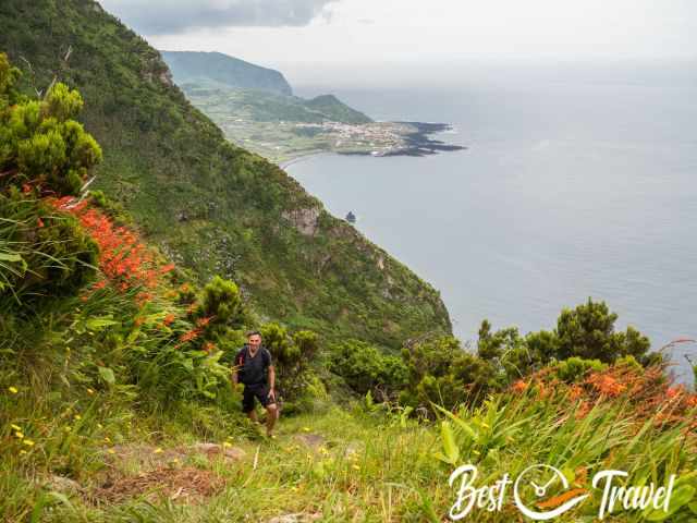 A hiker at higher elevation with orange flowers to the right and left..