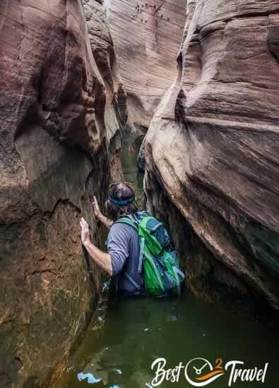 A hiker waist deep in murky green water in Zebra Slot