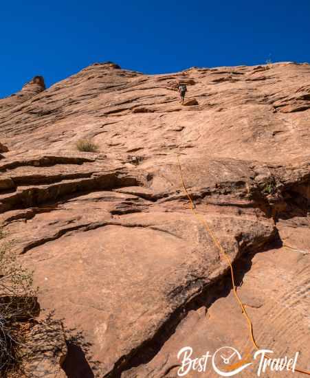 The steep wall and rope and a hiker climbing down