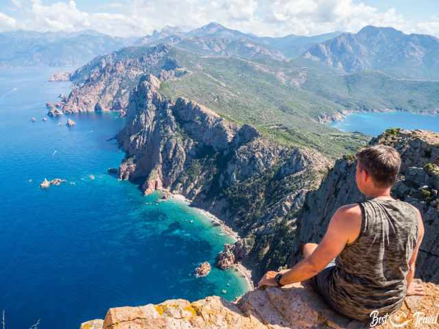 Ein Wanderer sitzt auf einer Klippe mit Blick auf das Meer.