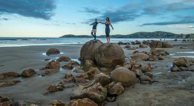 Two women posing on top of two Moeraki Boulders