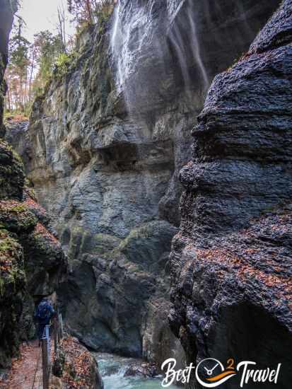 Zwei Besucher auf dem schmalen Klammweg und ein Wasserfall zur Rechten