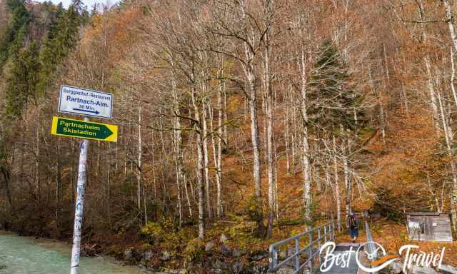 Wanderwegschilder und Brücke zur Partnachalm mit Herbstlaub.