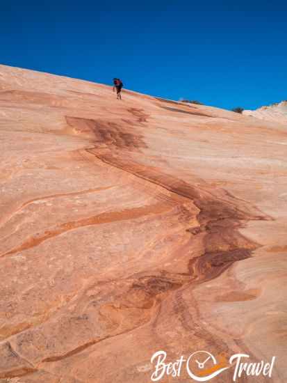 A hiker ascending Yellow Rock along a reddish pattern.
